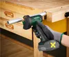 A person wearing a glove is using a cordless angle grinder to cut a metal pipe on a wooden workbench. Produktbild-Vorschau