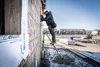 A construction worker is using a green multi-functional telescopic ladder to work on the exterior of a house under construction. Podgląd zdjęcia produktu