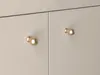 Close-up view of two gold cabinet knobs on a light-colored cabinet. Podgląd zdjęcia produktu