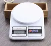 A white digital kitchen scale is placed on a wooden table next to a small wooden box. Voir les images du produit