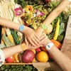 A group of people's arms are stacked on top of each other, each wearing a colorful watch, surrounded by fresh produce and flowers. Produktbild-Vorschau