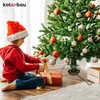 A child in a Santa hat is wrapping a gift next to a decorated Christmas tree. Náhled obrázku produktu