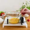 A person is using a device to whisk eggs in a glass bowl, with other kitchen items in the background. Produktbild-Vorschau