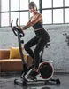 A woman is exercising on a stationary bike in a living room setting. Produktbild-Vorschau