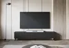 A modern living room setup featuring a large television mounted above a black TV cabinet. A floor lamp stands to the left, and the room has a minimalist aesthetic with wood-paneled accents on the wall. Náhled obrázku produktu