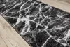 A close-up view of a marble-patterned rug on a wooden floor. Voir les images du produit