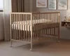 A wooden baby crib with bedding is shown in a room with artwork on the wall and curtains. Anteprima dell’immagine prodotto
