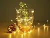 A glass mug filled with a small plant and wrapped in warm white LED string lights, with a pinecone on the side. Náhled obrázku produktu