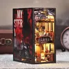 A 3D model of a book nook, designed to look like a scene from a mystery novel set on a train, is displayed on a surface with newspapers. Voir les images du produit