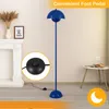 A blue floor lamp with a mushroom-shaped shade is shown in a room with a fireplace and a small table. A close-up of the foot pedal is also shown. Produktbild-Vorschau