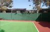 A tennis court with a green fence and trees in the background. Náhľad obrázku produktu