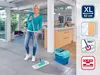 A woman is cleaning a floor with a mop in a modern living room. Produktbild-Vorschau