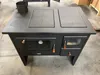 A black wood-burning stove with a metal cooktop and oven doors is shown in a workshop or storage area. Anteprima dell’immagine prodotto