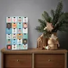 A wooden advent calendar with 24 drawers sits on a wooden dresser next to a vase of pine branches decorated with Christmas ornaments. Náhľad obrázku produktu