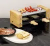 A raclette grill with food items on top and a plate of charcuterie and bread in the foreground. Produktbild-Vorschau