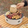 A hand holding a pitcher over a portable grill filled with various food items like sweet potatoes, nuts, and dates, set on a wooden table outdoors. Anteprima dell’immagine prodotto