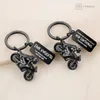 Two black motorcycle keychains with attached tags are displayed on a light-colored, textured surface. Produktbild-Vorschau