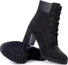 A pair of black Timberland heeled boots are shown against a white background. One boot is standing upright and laced, while the other is lying on its side, showing its sole. Podgląd zdjęcia produktu