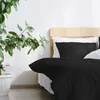 A bed with black bedding and white pillows, next to a potted plant. Produktbild-Vorschau