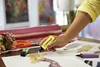 A person's hand is holding a yellow highlighter over fashion sketches on a table. Other highlighters and scissors are also visible. Anteprima dell’immagine prodotto
