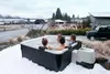 Four people relaxing in a hot tub in the snow, with a car and houses in the background. Náhľad obrázku produktu