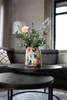 A colorful vase filled with flowers sits on a coffee table in a living room. Voir les images du produit