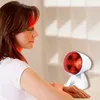 A woman is using a red infrared lamp for therapeutic purposes. Produktbild-Vorschau