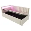 A beige upholstered daybed with its mattress support raised, revealing storage space underneath. Pink LED lights illuminate the headboard. Náhled obrázku produktu