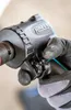 A gloved hand is adjusting a setting on a black power tool. Produktbild-Vorschau