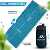 A teal sleeping bag is laid out diagonally on a white background with green foliage elements. A black mesh bag with the brand logo is shown to the right, with dimensions indicated. Produktbild-Vorschau