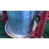 A close-up of a stainless steel fruit mill with juice and pulp collecting in a bowl below, set against a grassy background. Produktbild-Vorschau