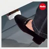 A person's foot in a black shoe is pressing down on a silver pedal attached to a white surface. Anteprima dell’immagine prodotto