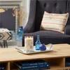 A lit candle and decorative bottles are placed on a tray on a coffee table in front of a dark blue armchair. Voir les images du produit