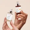 Two hands hold up two bottles of Avène skincare serum against a light beige background. Anteprima dell’immagine prodotto