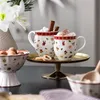 Two mugs filled with hot beverages and toppings, a bowl of nuts, and cookies are arranged on a table, suggesting a cozy winter setting. Náhled obrázku produktu