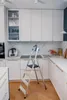 A kitchen with white cabinets and marble countertops, featuring a silver and black stepladder in the center. Náhled obrázku produktu