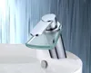 A modern chrome faucet with a glass waterfall spout sits atop a white sink. Produktbild-Vorschau