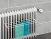 A white towel rack is attached to a white radiator, holding two folded towels. The radiator is mounted on a tiled wall. Produktbild-Vorschau