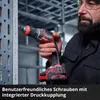 A man is holding a cordless drywall screw gun, with a metal shelving unit in the background. Voir les images du produit