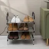 A three-tier shoe rack filled with various shoes, placed against a light-colored wall with shadows. Produktbild-Vorschau