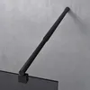 A black shower support arm attached to a glass shower panel, against a concrete wall. Produktbild-Vorschau