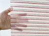 A hand is holding a piece of fabric with horizontal stripes. Produktbild-Vorschau