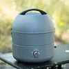 A portable gas grill sits on a table outdoors with a blurred green and yellow background. Produktbild-Vorschau