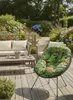 A cozy outdoor seating area with a sofa, coffee table, and a unique patterned chair, surrounded by lush greenery and flowers. Produktbild-Vorschau