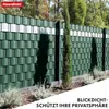 A green privacy fence with white accents, set in an outdoor garden with trees and plants in the background. Podgląd zdjęcia produktu