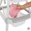 A hand is placing a pink cloth into a storage basket under a high chair. Anteprima dell’immagine prodotto