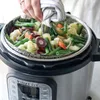 A person is using a steamer basket to remove cooked vegetables from an Instant Pot. Produktbild-Vorschau