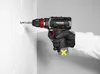 A person wearing gloves is using a cordless drill to make a hole in a white tiled wall. Produktbild-Vorschau