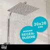 A square shower head with water spraying from it, set against a tiled wall. Two blue circular overlays provide product information. Produktbild-Vorschau