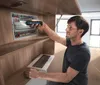 A man is using a cordless screwdriver to work on an electrical panel inside a wooden cabinet. Voir les images du produit